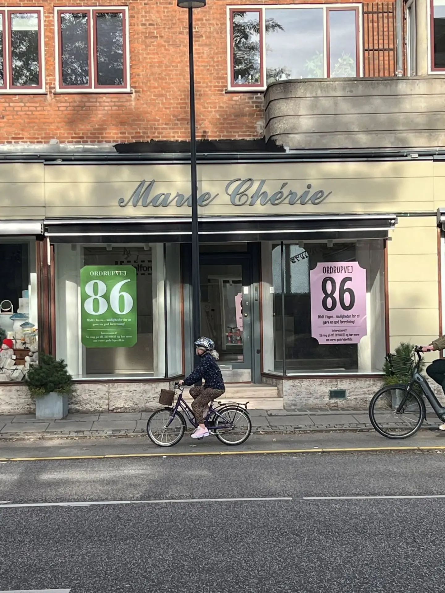 Butiksfacade med “Til leje”-plakater i grønne og lyserøde vinduesfolier, hvor der står Ordrupvej 86 og kontakttelefon – et eksempel på vinduesfolie til et ledigt erhvervslejemål.