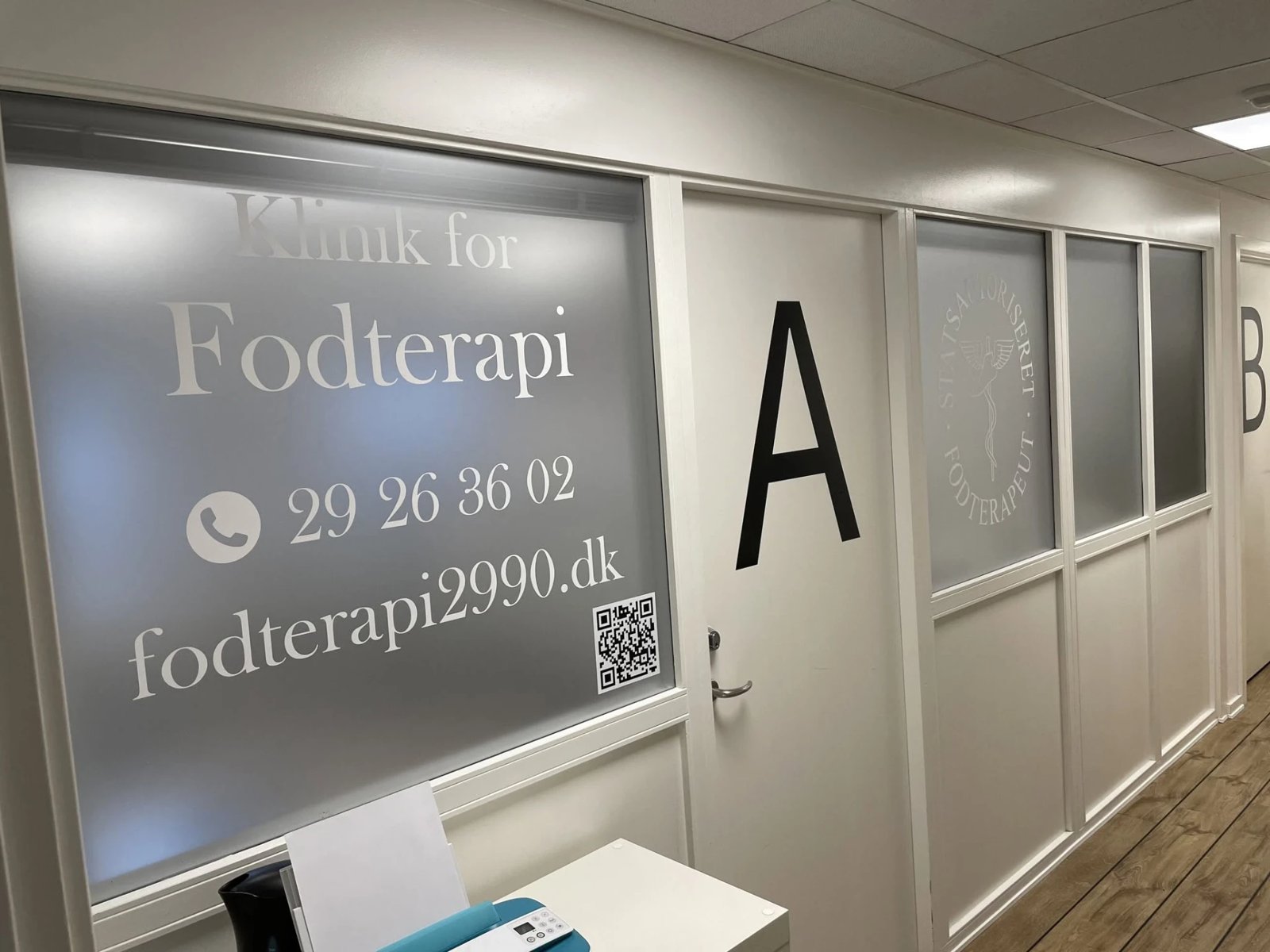 Frosted folie på klinikvindue med trykt åbningstider og kontaktinfo